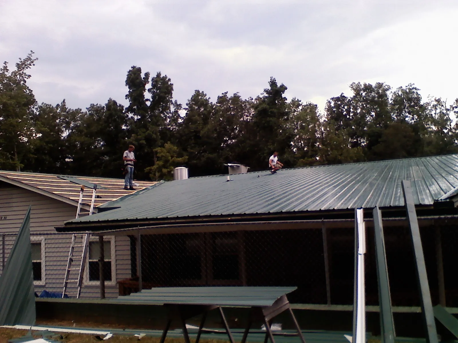 Two roofers installing green metal panels above a covered porch in Atlantic